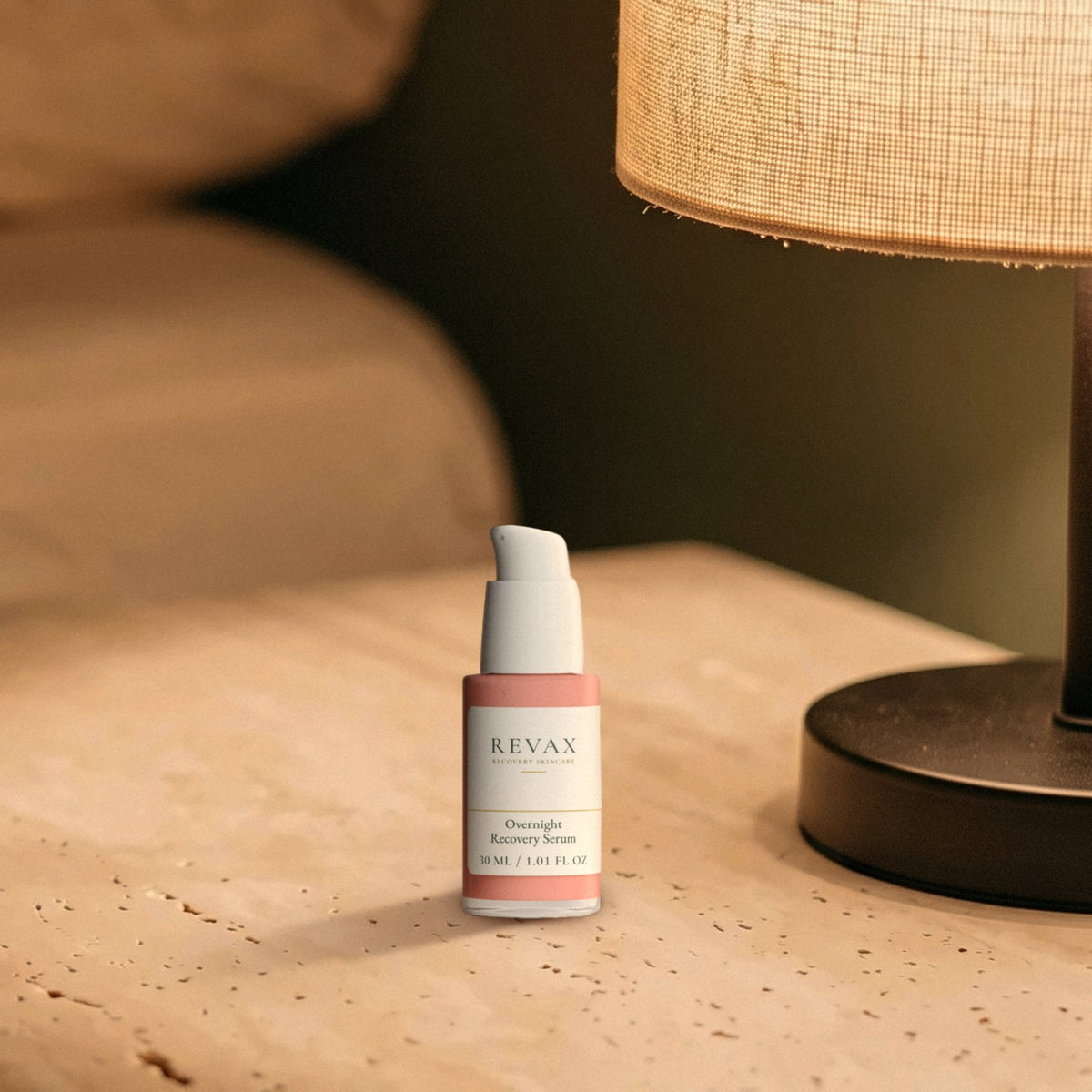 REVAX Overnight Recovery Serum 30 ml, pump bottle on a travertine nightstand beside a lit lamp at night, front view
