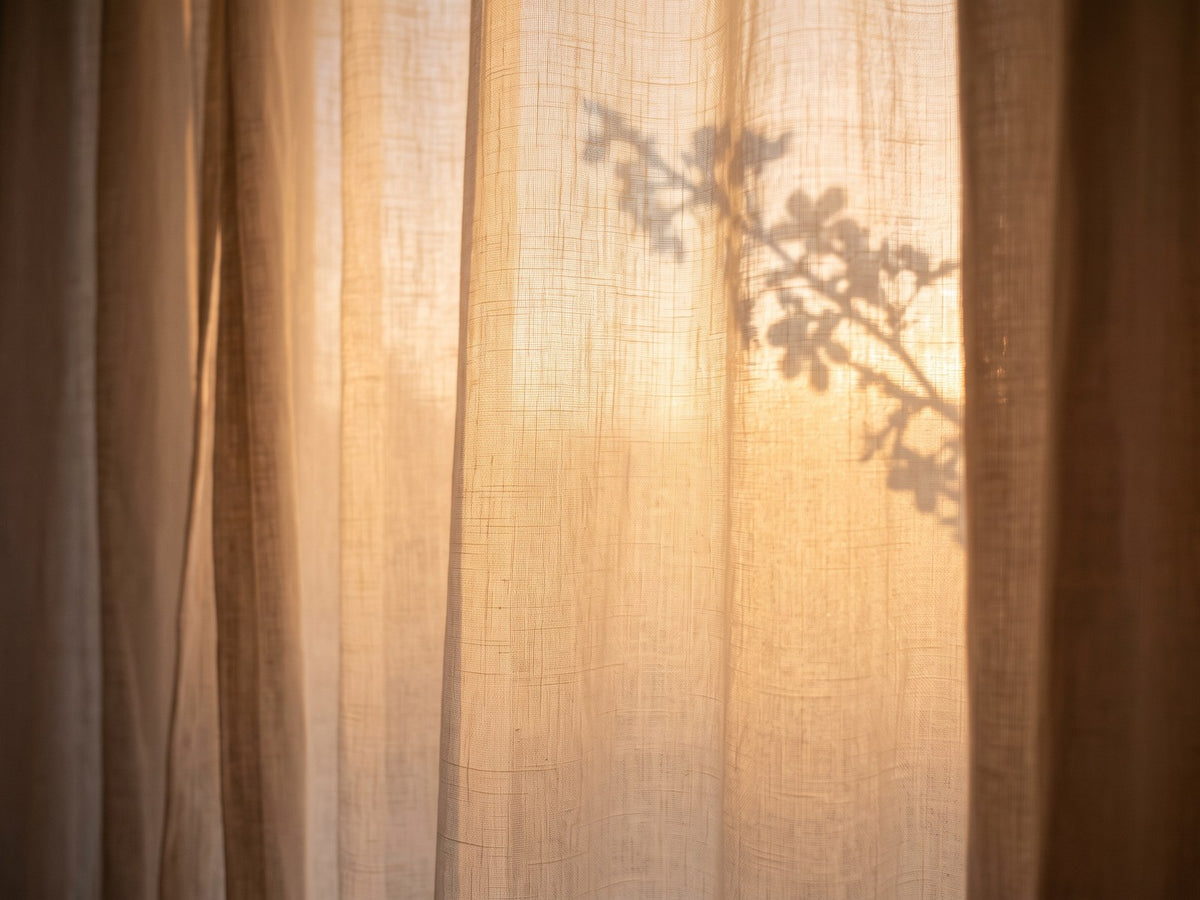 Sheer linen curtain glowing in warm evening light, with the soft shadow of a blossoming branch