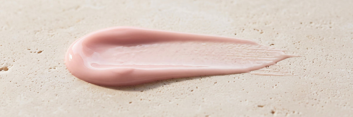 REVAX Overnight Recovery Serum texture, a swipe of the pale pink serum on cream travertine stone